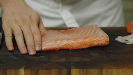 Close-up-of-chef-peeling-salmon-fillet-on-wooden-board-in-kitchen---Descale-Skin-From-Salmon-Fillet-With-A-Sharp-Knife