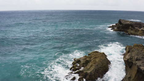 Foamy-Waves-Crashing-Against-Rocks-At-La-Poza-del-Obispo-Beach-In-Arecibo,-Puerto-Rico---aerial-drone-shot