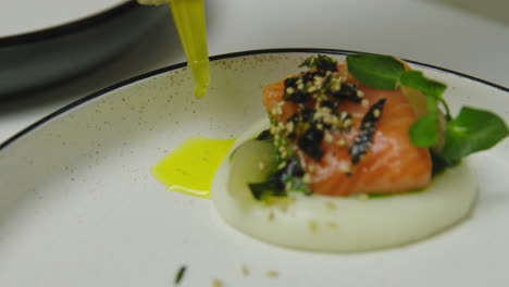 Close-up-of-chef-dropping-olive-oil-on-plate-beside-salmon-meal-in-restaurant