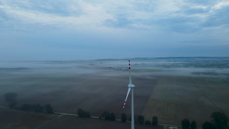 4k-Antenne:-Ruhige-Windkraftanlage-Und-Mystischer-Nebel,-Der-Früh-Morgens-Vor-Sonnenaufgang-über-Landwirtschaftlichen-Feldern-In-Polen-Schwebt