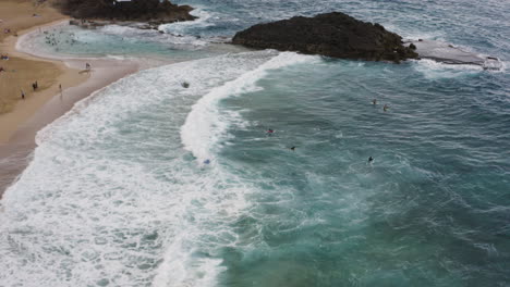 Foamy-Waves-Of-Blue-Ocean-With-Tourists-Enjoying-At-La-Poza-del-Obispo-Beach-In-Arecibo,-Puerto-Rico---aerial-drone-shot