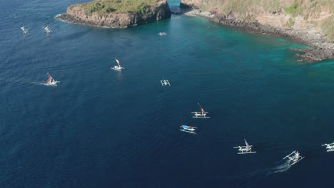 Wooden-Cadik-fishing-boats-moving-in-blue-water-towards-rocky-shore-of-Bali,-aerial