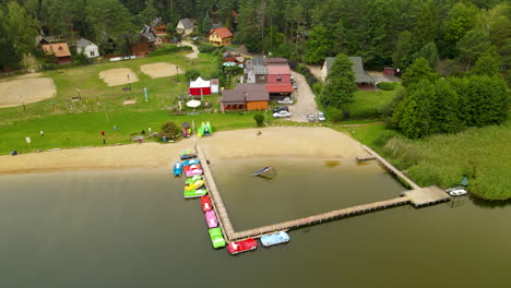 Aerial-shot-of-natural-Lake-with-sandy-beach,-volleyball-field-and-shore-in-green-landscape---Hartowiec,Poland
