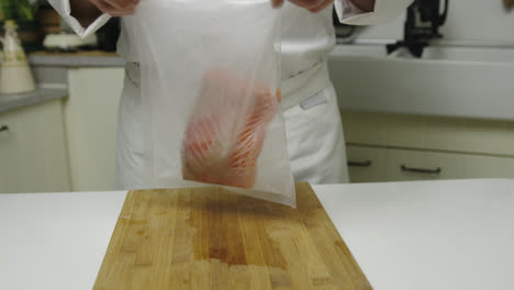 Close-up-shot-of-male-chef-putting-fresh-salmon-fillet-into-airtight-bag-in-kitchen