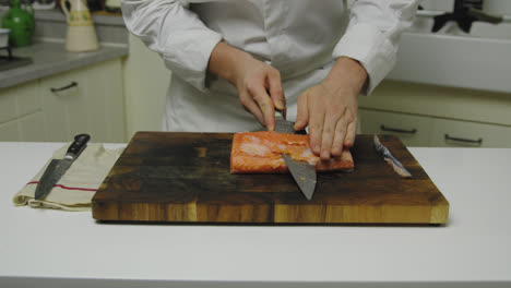 Starred-Chef-cutting-fresh-salmon-fillet-into-slices-on-wooden-board,close-up