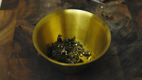 Close-up-of-chef-putting-fresh-cutting-seaweed-into-golden-bowl,slow-motion
