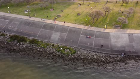Luftaufnahme-Von-Menschen,-Die-Sich-Auf-Der-Wiese-Entspannen,-Fahrrad-Fahren-Und-Am-Flussufer-Des-Rio-De-La-Plata,-Buenos-Aires-Spazieren-Gehen