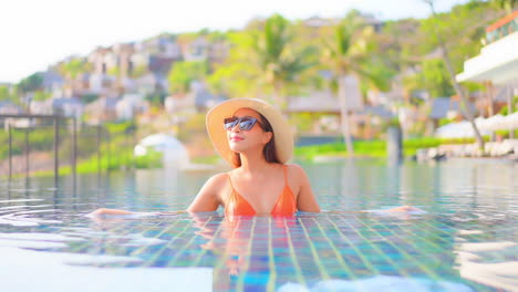 American-Woman-in-Orange-Bikini-Raising-Hands-Up-Inside-Tropical-Swimming-Pool-in-Santorini-Greece,-Happy-Traveler-on-Vacation,-slow-motion-handheld