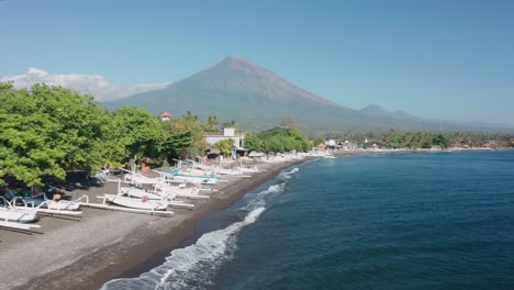 Amed-Beach-with-traditional-white-jukung-outrigger-boats,-Mount-Agung,-aerial