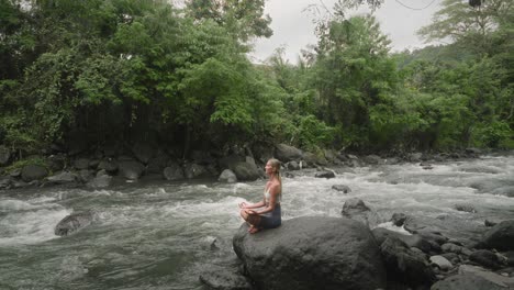 Blond-millennial-woman-during-nature-healing-in-Sukhasana-easy-pose-on-rock