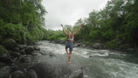 Young-woman-doing-yoga-tree-pose,-tropical-river-in-Indonesia,-slowmo