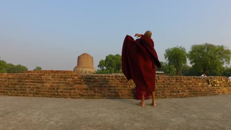 Ein-Buddhistischer-Mönch-Hüllt-Seine-Chivara-Mit-Blick-Auf-Die-Dhamek-Stupa-In-Varanasi,-Indien