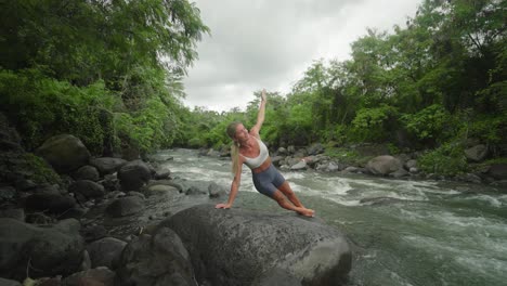 Fit-sportive-young-woman-doing-Side-Plank-pose-on-rock-beside-river,-Vasisthasana