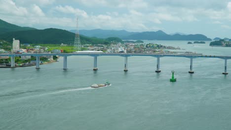 A-bridge-joins-Geojedo-Island-to-the-South-Korean-mainland-with-a-barge-pulling-cargo---static,-wide-angle-view