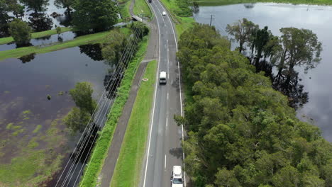 4k-Drone-shot-of-cars-driving-on-a-small-road-next-to-a-big-flood-at-Byron-Bay,-Australia