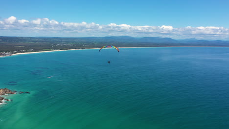 4k-Wide-drone-shot-of-a-man-paragliding-over-the-ocean-sea-at-Byron-Bay,-Australia