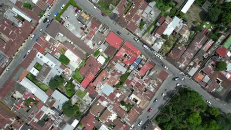 Drohnen-Luftaufnahmen-Des-Straßenverkehrs-Von-Autos-Und-Motorrädern-In-Antigua,-Einer-Kolonialstadt-In-Guatemala,-Mit-Leuchtend-Bunten-Roten-Dächern-Und-Grünen-Baumkronen