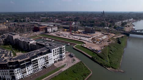 Aerial-approach-and-passing-of-luxury-apartment-building-and-construction-site-of-Kade-Zuid-complex-on-the-other-side-of-recreational-port-with-tower-town-Zutphen-in-the-background-on-a-sunny-hazy-day