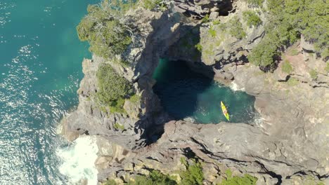 Kayakers-exploring-beautiful-rock-formation-arch-at-shore-of-New-Zealand,-aerial