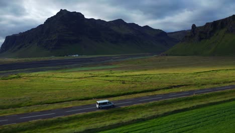 Vehículos-Circulando-Por-La-Carretera-En-Islandia-Con-Montaña-Rocosa-En-Segundo-Plano