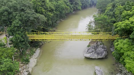Drone-aerial-footage-of-yellow-bridge-over-river-Rio-Cahabon-near-Semuc-Champey-National-Park-in-Guatemala-surrounded-by-bright-green-rainforest-trees-near-Chicanutz