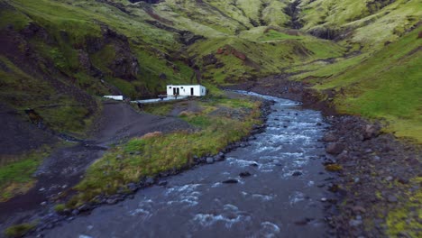 Volando-Sobre-El-Río-Que-Fluye-En-El-Valle-Hacia-La-Piscina-Seljavallalaug-En-Islandia