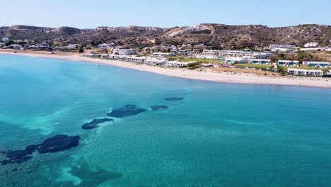 Cinematic-drone-shot-of-paradisiacal-greek-beach-with-a-beautiful-sea-and-some-houses-on-the-shore