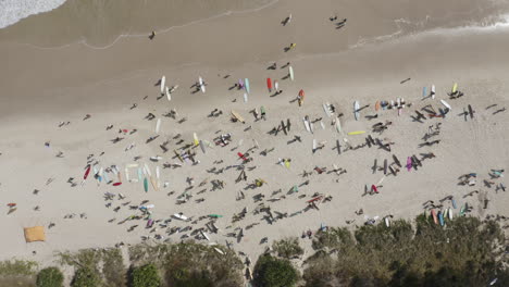 4k-Drone-shot-of-surfer-people-with-their-surfboards-standing-on-the-beautiful-white-beach-at-Byron-Bay,-Australia