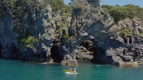 Kayaking-beside-rock-arch-on-Moutohora-Whale-Island-shore,-sunny-day