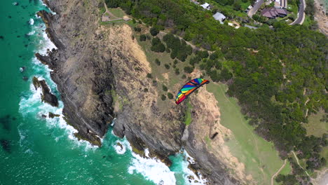 4k-Drone-shot-over-a-paraglider,-flying-over-mountains-and-the-shore-at-Byron-Bay,-Australia
