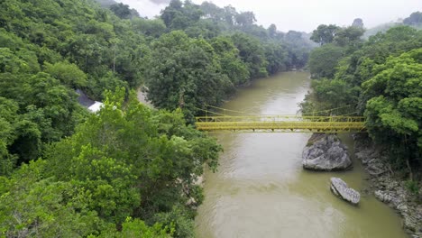 Drohne-Luftaufnahmen-Der-Gelben-Brücke-über-Den-Fluss-Rio-Cahabon-In-Der-Nähe-Des-Semuc-Champey-Nationalparks-In-Guatemala,-Umgeben-Von-Hellgrünen-Regenwaldbäumen-In-Der-Nähe-Von-Chicanutz