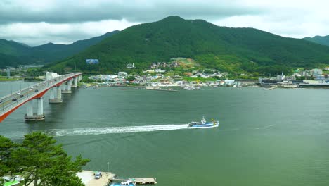 Neue-Geoje-Grand-Bridge-Mit-Fahrzeugen,-Die-Nach-Tongyeong-Reisen,-Und-Einem-Schiff,-Das-Das-Küstengebiet-Mit-Blick-Auf-Die-üppig-Grünen-Berge-Auf-Der-Geojedo-insel,-Südkorea,-überquert