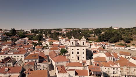 Panoramic-aerial-pan-shot-of-Santiago-church-and-parish-townscape-in-Alcacer-Do-Sal,-Portugal