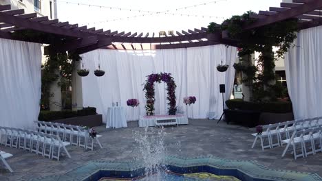 Drone-flying-towards-wedding-stage,-wedding-ceremony-under-the-open-sky-and-a-fountain-at-the-center-of-the-stage