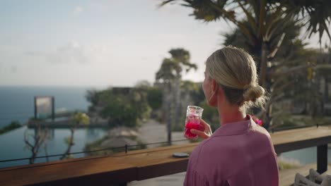 Woman-grabs-tropical-drink-from-table,-sipping-cocktail-and-enjoys-ocean-view