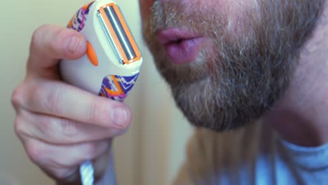Little-handheld-electric-razor-being-blown-out-by-blonde-honey-bearded-white-caucasian-man
