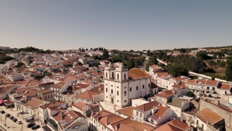 Historical-church-with-two-towers-and-majestic-cityscape-of-Alcacer-Do-Sal-town-in-Portugal,-aerial-drone-view
