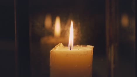 Close-up-of-candle-flame-burning-inside-glass-latern-at-night