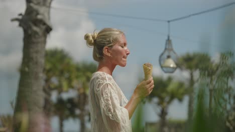 Pretty-blond-woman-in-trendy-white-dress-taking-bite-from-ice-cream,-holiday