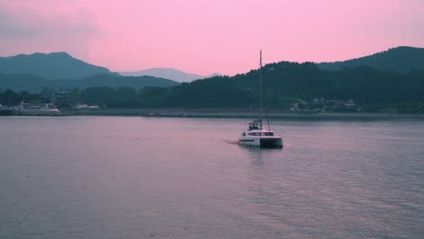 Catamaran-Boat-With-Tourists-Leisurely-Sailing-At-Dusk-With-Bright-Pink-Sky-In-South-Korea