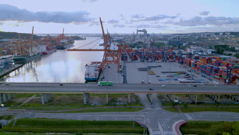 Gdynia-Frachthof-Hafen,-Große-Kräne,-Die-Fracht-Auf-Containerschiffe-In-Der-Dämmerung-Laden,-Lastwagen,-Der-Sich-Bei-Sonnenuntergang-Entlang-Der-Brücke-Bewegt