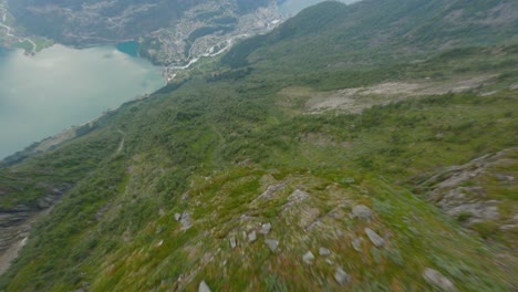 Aerial-flight-downhill-green-mountains-towards-tourist-town-Odda-and-Fjord-in-Norway---FPV-Dynamic-drone-shot---Freimstolen-Rossnos-Mountain