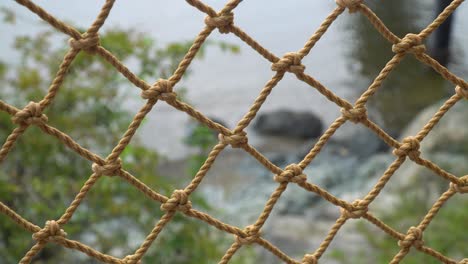 Close-Up-Of-Rope-Net-Fence-With-Blurred-Ocean-In-The-Background