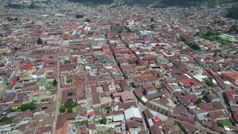Drone-aerial-footage-of-urban-central-american-city-Quetzaltenango,-Xela,-Guatemala-showing-colorful-red-rooftops-and-streets