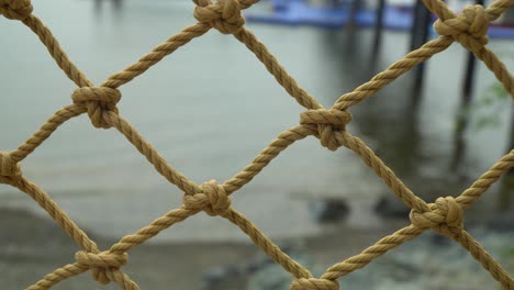Rope-Net-Fence-On-Seashore-Of-Beach-With-Calm-Water-In-The-Background