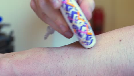 Little-handheld-electric-razor-white-with-purple-and-orange-design-pattern,-shaving-the-forearm-of-a-white-caucasian-man-or-women-with-freckles-on-arm