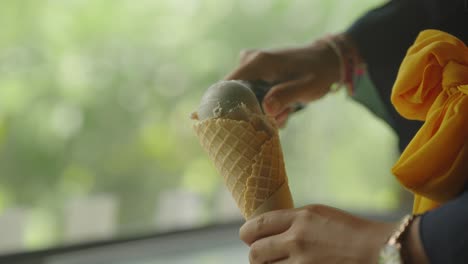 Hands-holding-pastry-cone-scooping-ball-of-ice-cream-with-spoon,-close-up