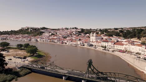 Puente-Elevador-Sobre-El-Río-Sado-Con-Majestuosa-Vista-Del-Horizonte-De-La-Ciudad-De-Alcacer-Do-Sal,-Antena