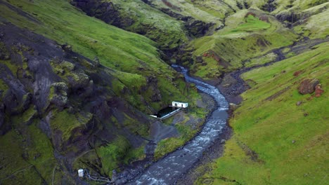 Aerial-View-Of-Famous-Seljavallalaug-Swimming-Pool-On-Foothill-Of-Mountain-With-River-In-Iceland