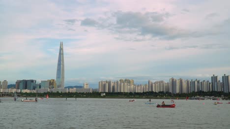Seoul-City-Skyline---People-kayaking,-riding-windsurfing,-paddleboarding-at-Han-river,-Seoul-downtown-on-colorful-pinky-sunset,-Lotte-World-Tower-on-Background